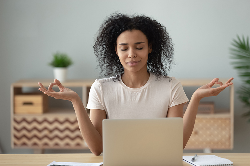 African woman meditating sitting at desk in front of laptop